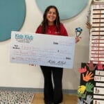 Smiling Kids Klub staff holding oversized check and trophy, celebrating EnrichEd enrichment in a supportive community space.
