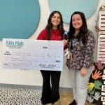 Two smiling staff hold a giant check and trophy in a kids enrichment room, celebrating achievement — EnrichEd.