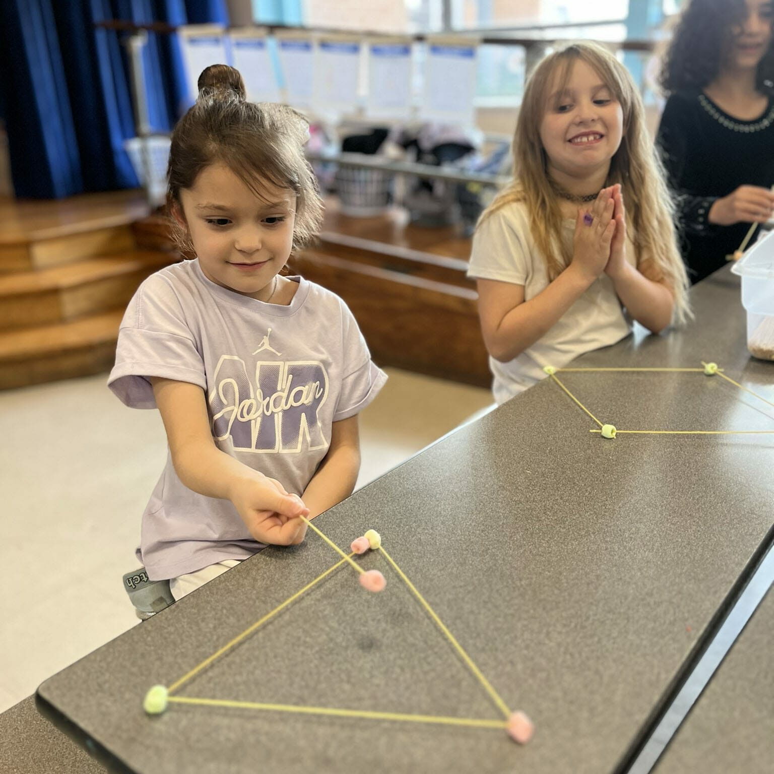 Two girls build triangular shapes with yellow sticks and small foam connectors in an EnrichEd enrichment activity.