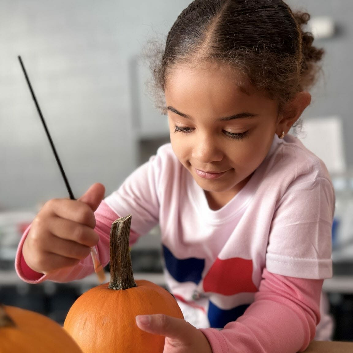 Young girl painting a pumpkin in an EnrichEd craft, showing creative learning and community support.