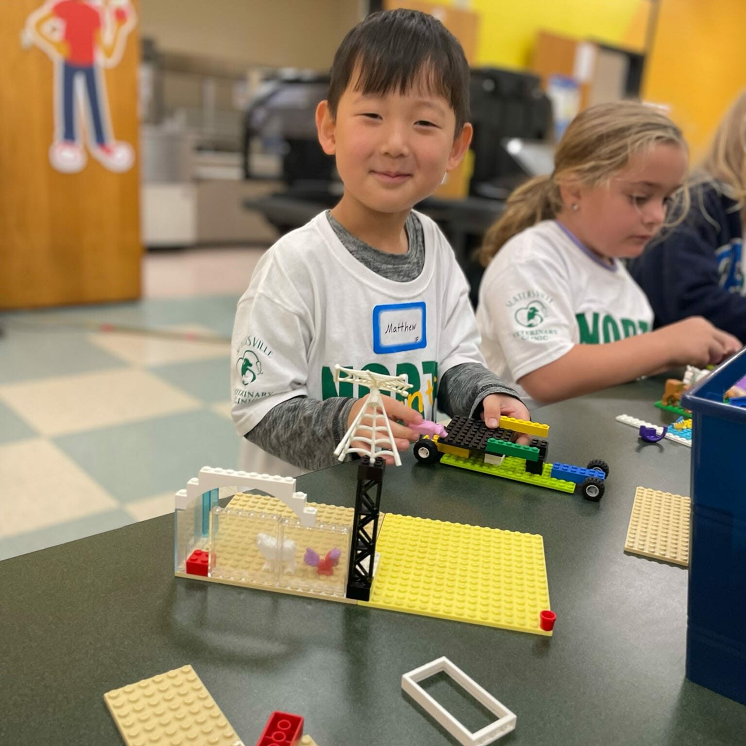Smiling boy and classmates building LEGO models at a table in a safe EnrichEd program environment, learning together.