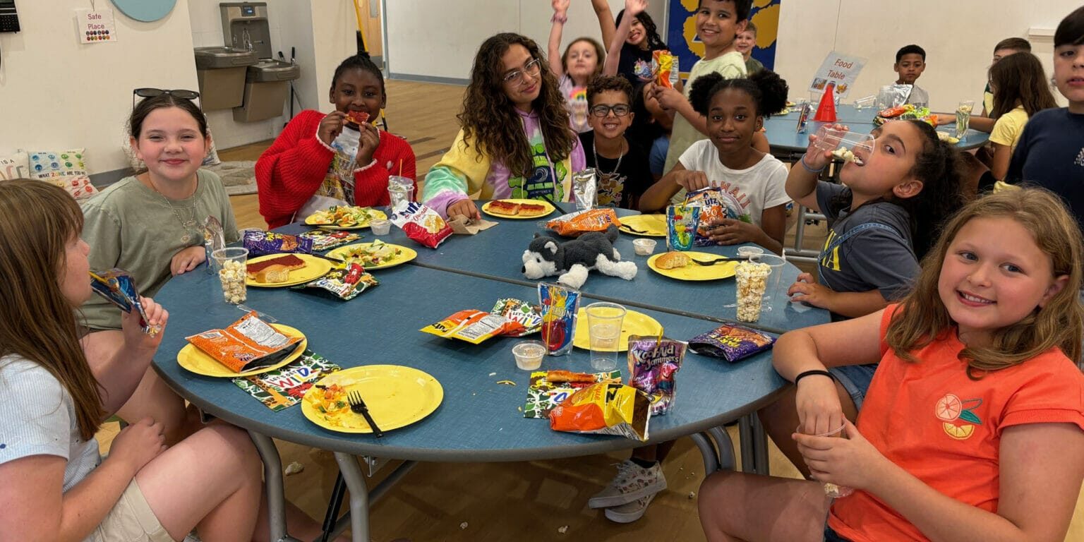 enhanced-food-meals Children gathered around a cafeteria table enjoying snacks and laughter in a safe, supportive EnrichEd program.