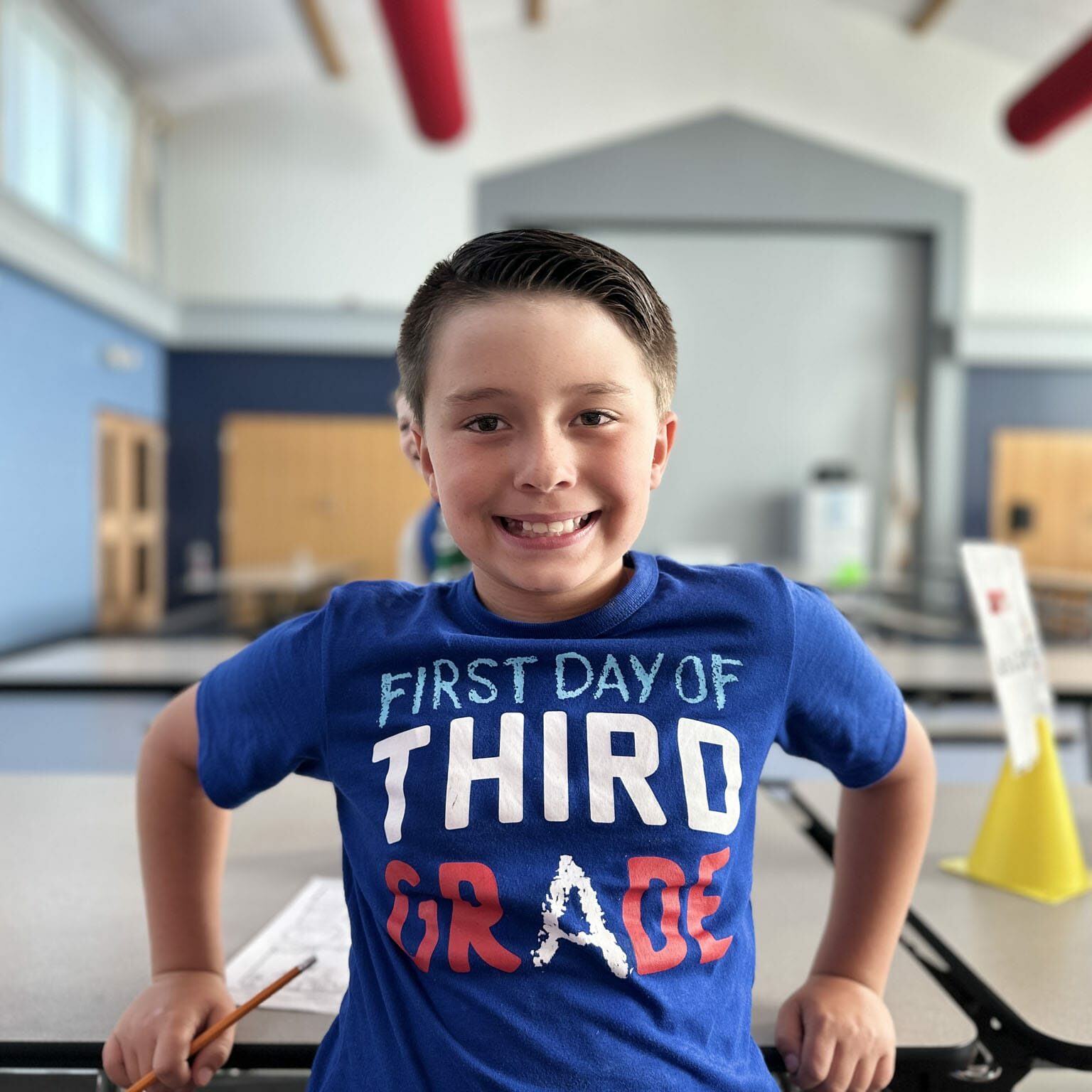 EnrichEd student smiling at a table, holding a pencil and ready for third-grade activities during after-school program.